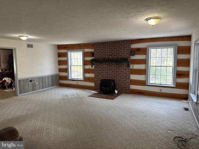 unfurnished living room with a wood stove, a textured ceiling, carpet flooring, and visible vents