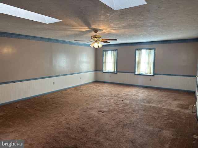 spare room featuring a textured ceiling, carpet flooring, crown molding, a wainscoted wall, and a skylight