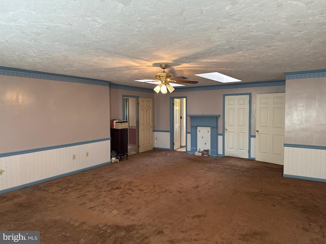unfurnished living room featuring carpet, a skylight, baseboards, wainscoting, and ceiling fan
