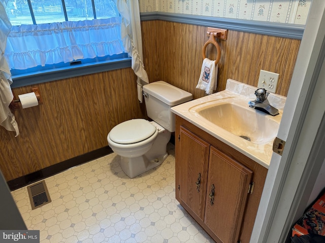 bathroom featuring toilet, vanity, and wooden walls