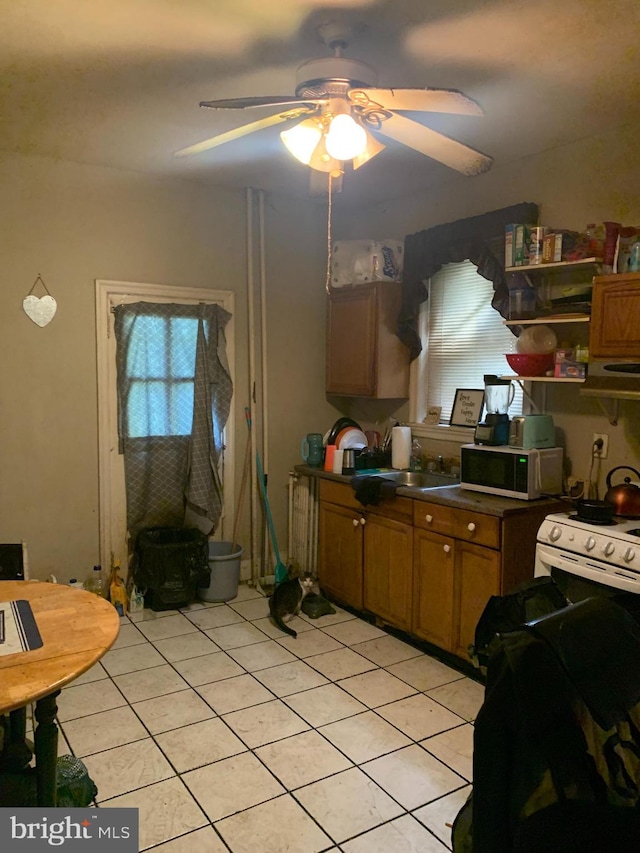 kitchen featuring sink, light tile patterned floors, ceiling fan, and white gas range oven