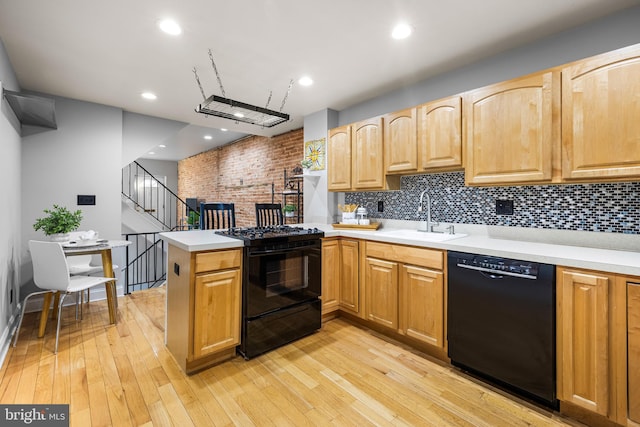 kitchen with black appliances, kitchen peninsula, sink, and light hardwood / wood-style flooring