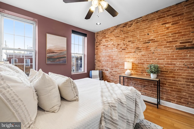 bedroom featuring hardwood / wood-style floors, ceiling fan, and brick wall