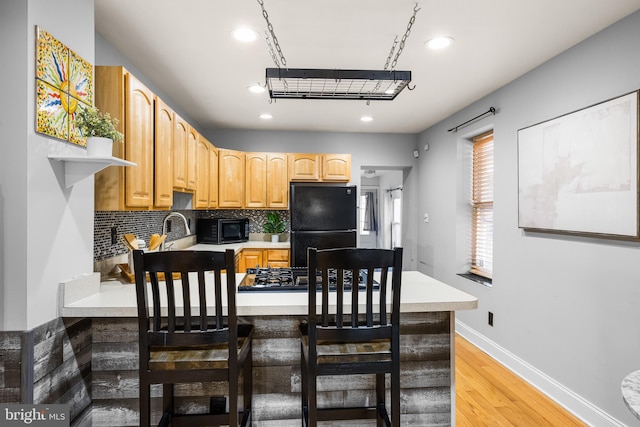 kitchen with a breakfast bar, black appliances, light brown cabinets, light wood-type flooring, and decorative backsplash