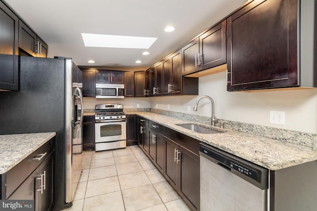 kitchen featuring light tile patterned flooring, sink, light stone counters, appliances with stainless steel finishes, and a skylight