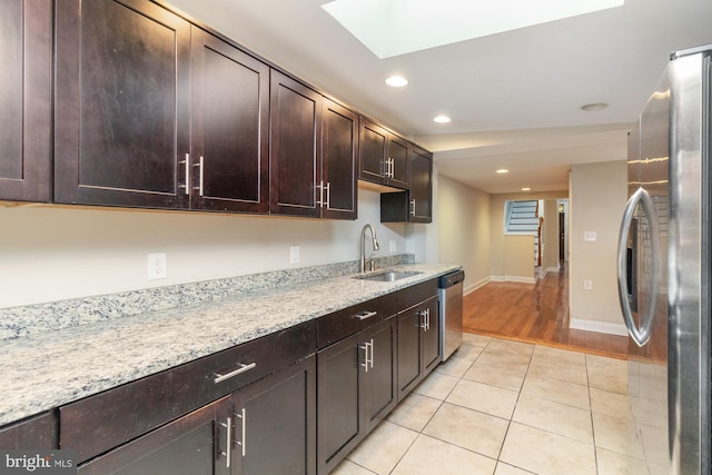 kitchen with stainless steel appliances, light stone countertops, light tile patterned floors, and sink