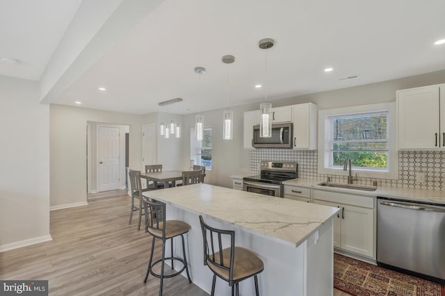 kitchen with appliances with stainless steel finishes, sink, pendant lighting, white cabinets, and a center island