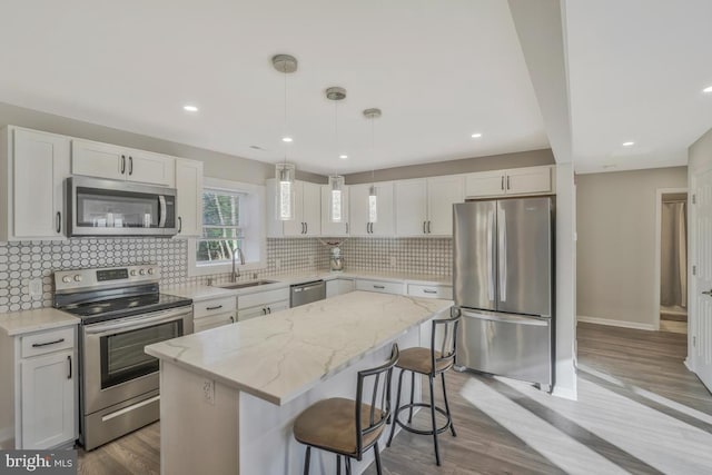 kitchen with a center island, hanging light fixtures, sink, appliances with stainless steel finishes, and white cabinetry