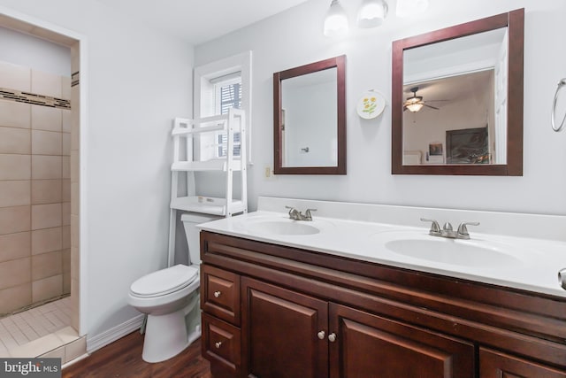 bathroom featuring tiled shower, vanity, hardwood / wood-style floors, toilet, and ceiling fan