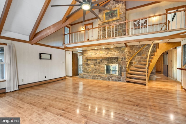 unfurnished living room featuring wood walls, ceiling fan, beam ceiling, high vaulted ceiling, and light hardwood / wood-style flooring