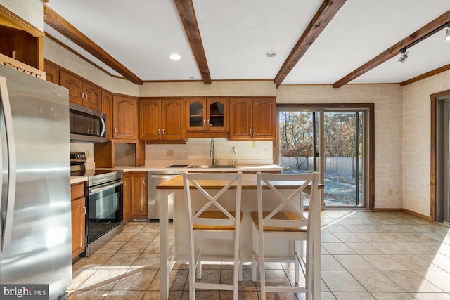 kitchen with stainless steel appliances, beamed ceiling, sink, and a kitchen breakfast bar