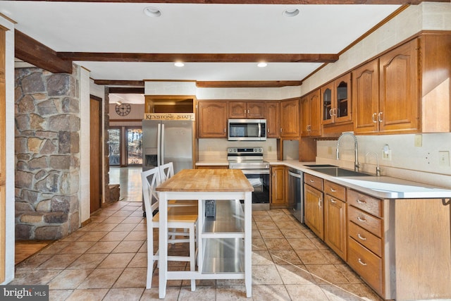 kitchen with appliances with stainless steel finishes, sink, a kitchen island, wood counters, and beam ceiling