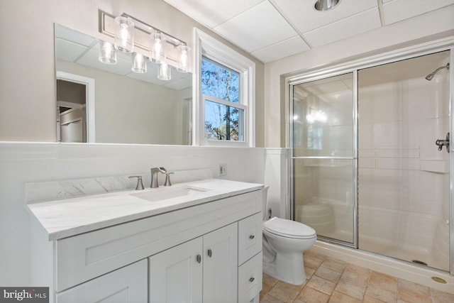 bathroom with a shower with door, vanity, a paneled ceiling, and toilet