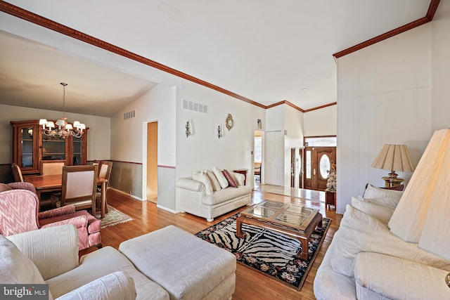 living room featuring an inviting chandelier, light hardwood / wood-style flooring, vaulted ceiling, and ornamental molding