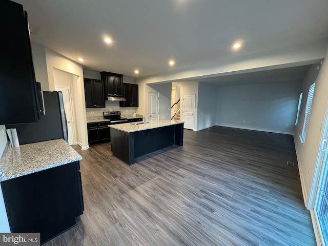 kitchen featuring black electric range oven, sink, hardwood / wood-style flooring, light stone countertops, and an island with sink