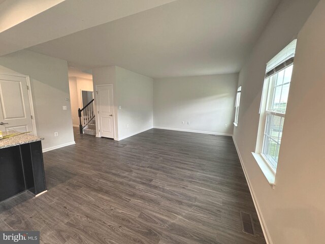 unfurnished living room with plenty of natural light, baseboards, and dark wood-style flooring