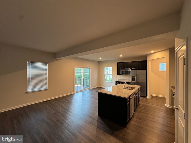 kitchen featuring light stone countertops, stainless steel appliances, sink, dark hardwood / wood-style floors, and an island with sink