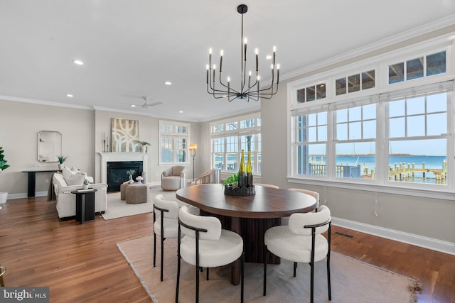 dining room featuring crown molding, a fireplace, a water view, and wood-type flooring