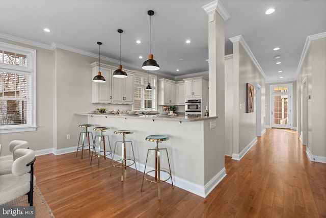 kitchen featuring stainless steel oven, kitchen peninsula, light hardwood / wood-style flooring, decorative light fixtures, and white cabinetry