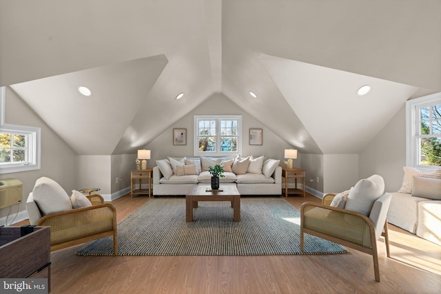 living room with a wall mounted air conditioner, a healthy amount of sunlight, vaulted ceiling, and light hardwood / wood-style floors