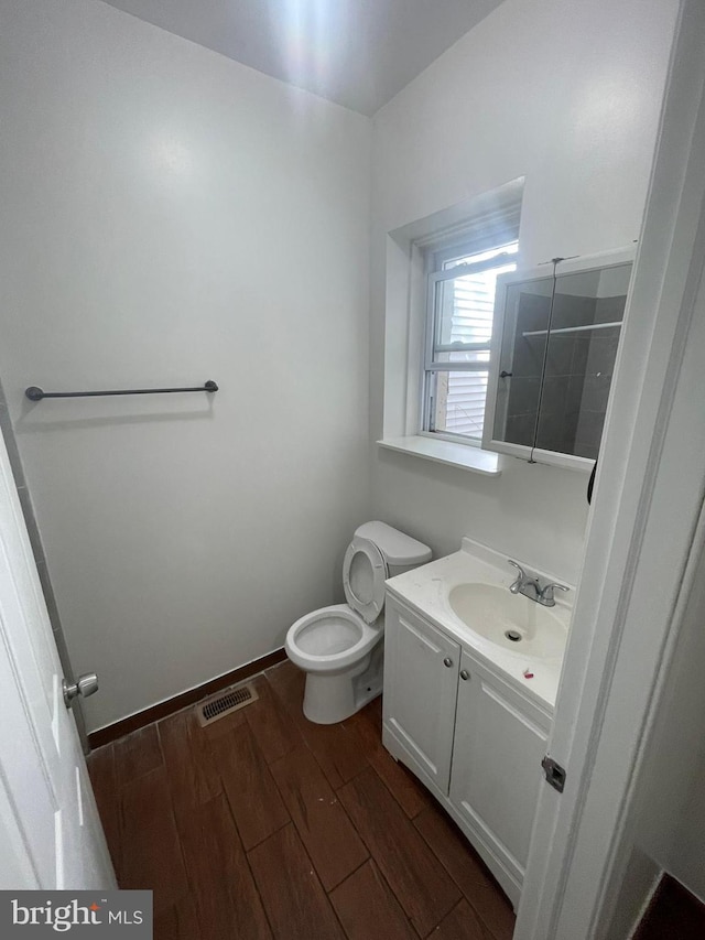 bathroom with toilet, wood finished floors, vanity, visible vents, and baseboards