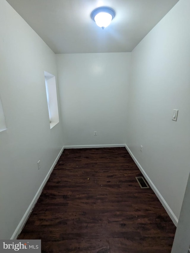 empty room featuring dark wood-style flooring, visible vents, and baseboards