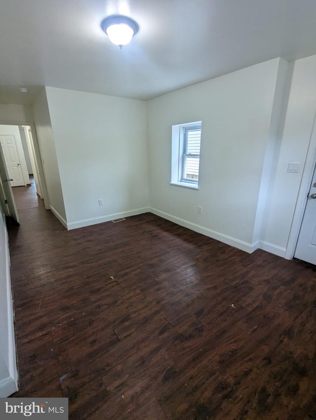 unfurnished room featuring dark wood-style floors, visible vents, and baseboards