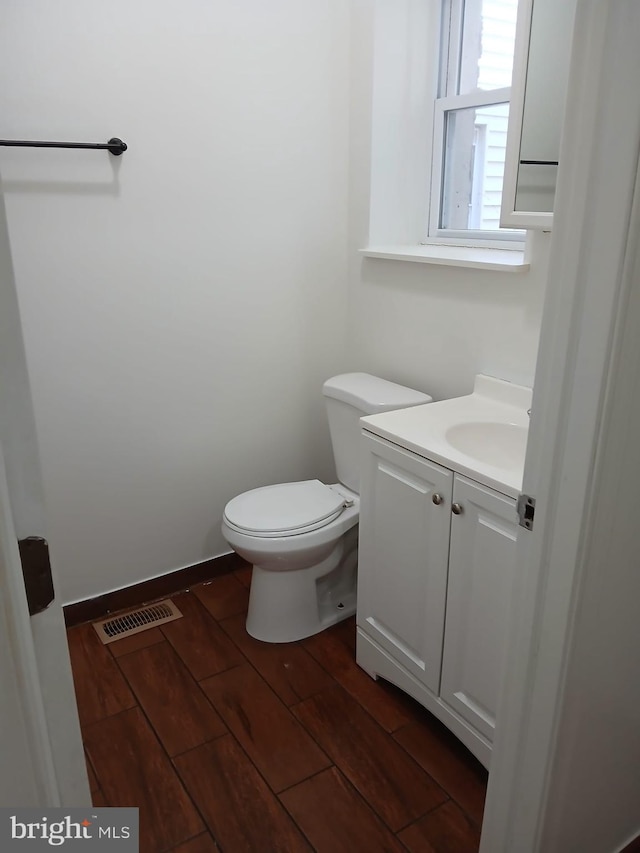 half bath with toilet, vanity, wood finished floors, and visible vents