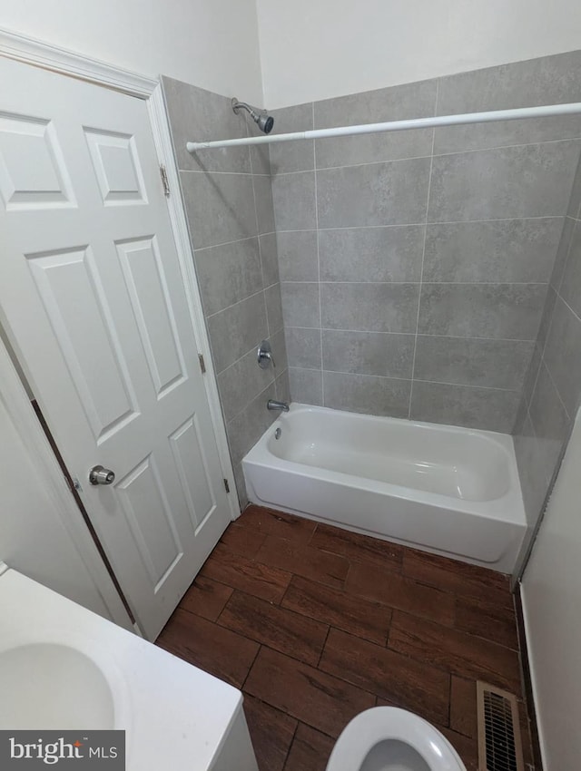 bathroom featuring visible vents, toilet, wood finished floors, bathtub / shower combination, and a sink