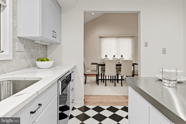 kitchen featuring light wood-type flooring, tasteful backsplash, vaulted ceiling, dishwasher, and white cabinetry