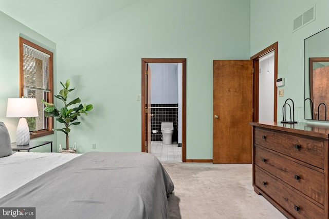 bedroom featuring light carpet, ensuite bathroom, and lofted ceiling