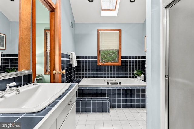 bathroom with tiled bath, vanity, a skylight, and tile patterned floors