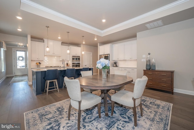 dining space with a raised ceiling, crown molding, dark wood-type flooring, and sink