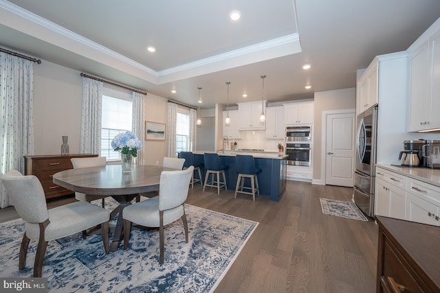 dining area with sink, a raised ceiling, crown molding, and dark wood-type flooring