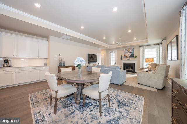 dining area featuring a raised ceiling, ceiling fan, dark wood-type flooring, and crown molding