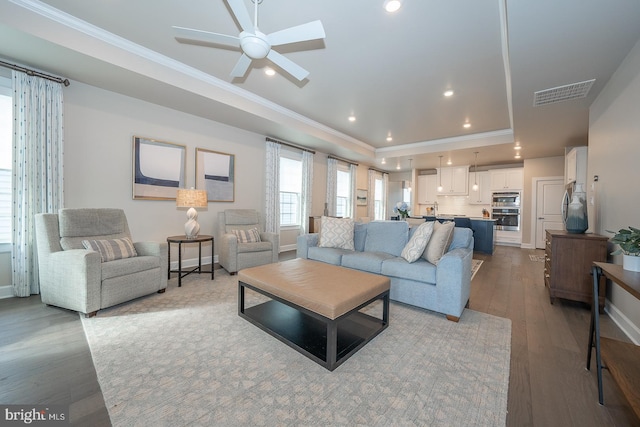 living room featuring a tray ceiling, crown molding, ceiling fan, and light hardwood / wood-style floors