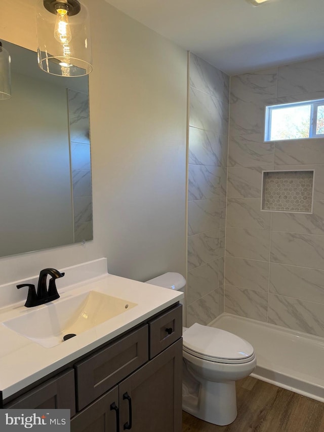 bathroom featuring vanity, a tile shower, hardwood / wood-style flooring, and toilet