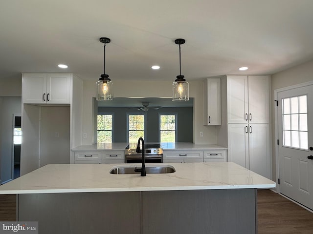 kitchen with light stone counters, sink, a center island with sink, and white cabinets