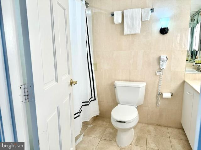 bathroom with a shower with shower curtain, vanity, tile patterned floors, toilet, and tile walls