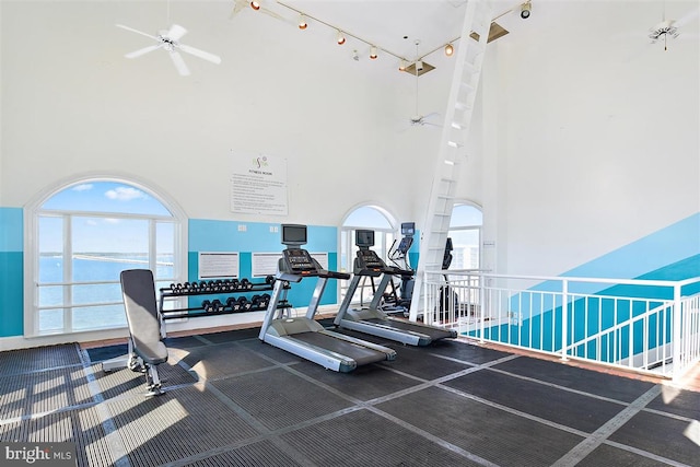 gym with a towering ceiling, ceiling fan, and a water view