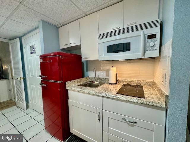 kitchen with fridge, white cabinetry, a drop ceiling, and sink