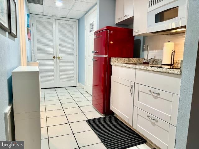 kitchen with sink, a drop ceiling, light tile patterned floors, fridge, and white cabinets