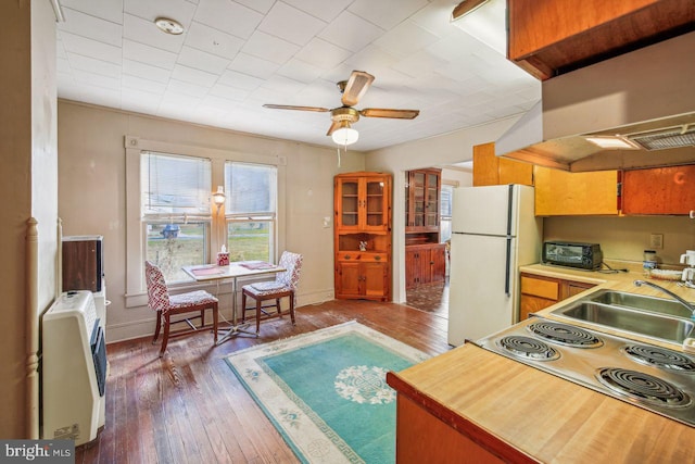 kitchen featuring hardwood / wood-style flooring, heating unit, white refrigerator, and range hood