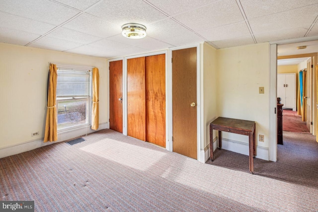 unfurnished bedroom with a drop ceiling, two closets, and carpet