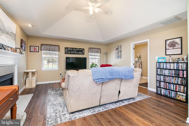 living room featuring a tile fireplace, dark hardwood / wood-style flooring, a raised ceiling, and ceiling fan