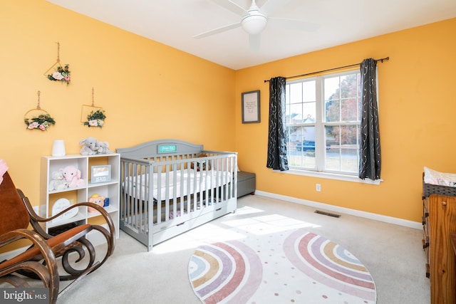 bedroom with a crib, light carpet, and ceiling fan