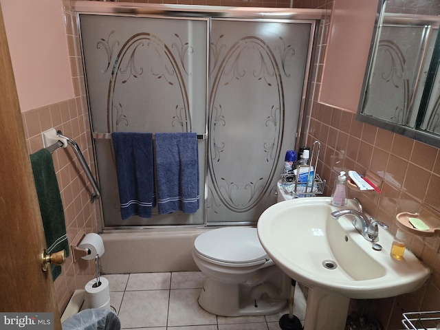 full bathroom with tile patterned flooring, bath / shower combo with glass door, tile walls, and toilet