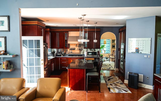 kitchen with decorative light fixtures, a kitchen bar, dark hardwood / wood-style flooring, an island with sink, and wall chimney exhaust hood