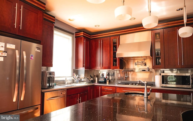 kitchen featuring stainless steel appliances, hanging light fixtures, decorative backsplash, sink, and wall chimney exhaust hood