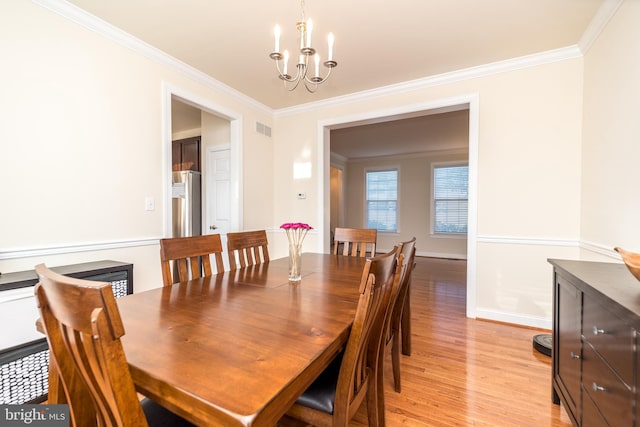 dining room featuring light wood-type flooring, a notable chandelier, and crown molding